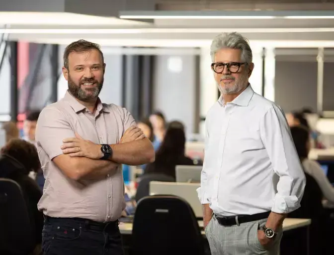 Os sócios-fundadores da Meu Contador Prime, Anderson Diógenes Pavanello (à esquerda) e Antonio André Neto (à direita), em destaque em um escritório moderno com equipe ao fundo.