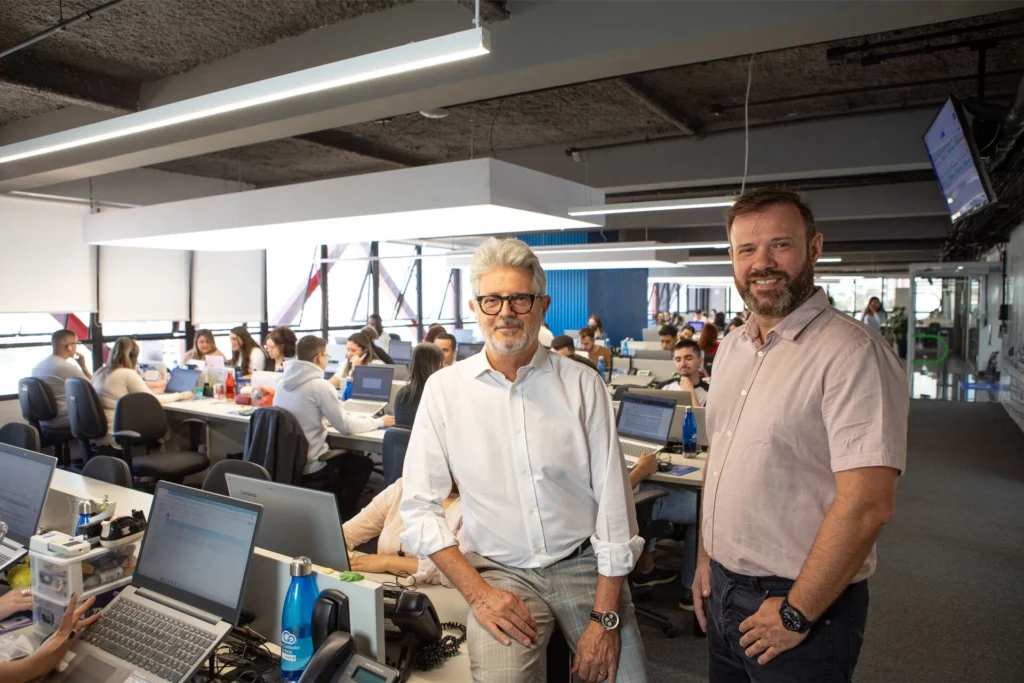 Escritório moderno da Meu Contador Prime com equipe trabalhando em ambiente colaborativo, tendo os sócios-fundadores Antonio André Neto (à esquerda) e Anderson Diógenes Pavanello (à direita) em destaque à frente.